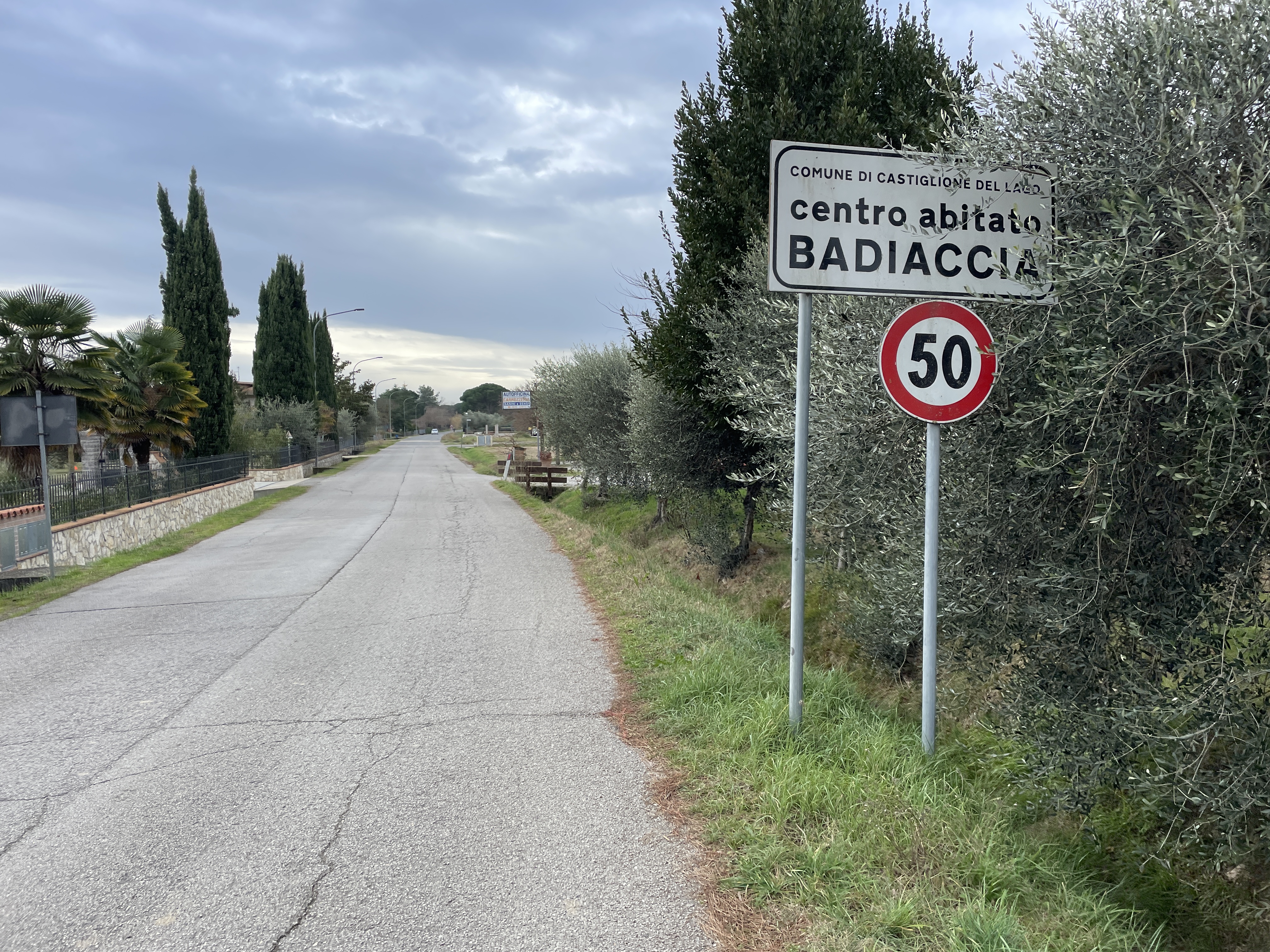 Abschnitt eines Radwegs auf einer asphaltierten Landstraße mit einem Straßenschild auf der rechten Seite, das den Eingang zum Dorf Badiaccia anzeigt